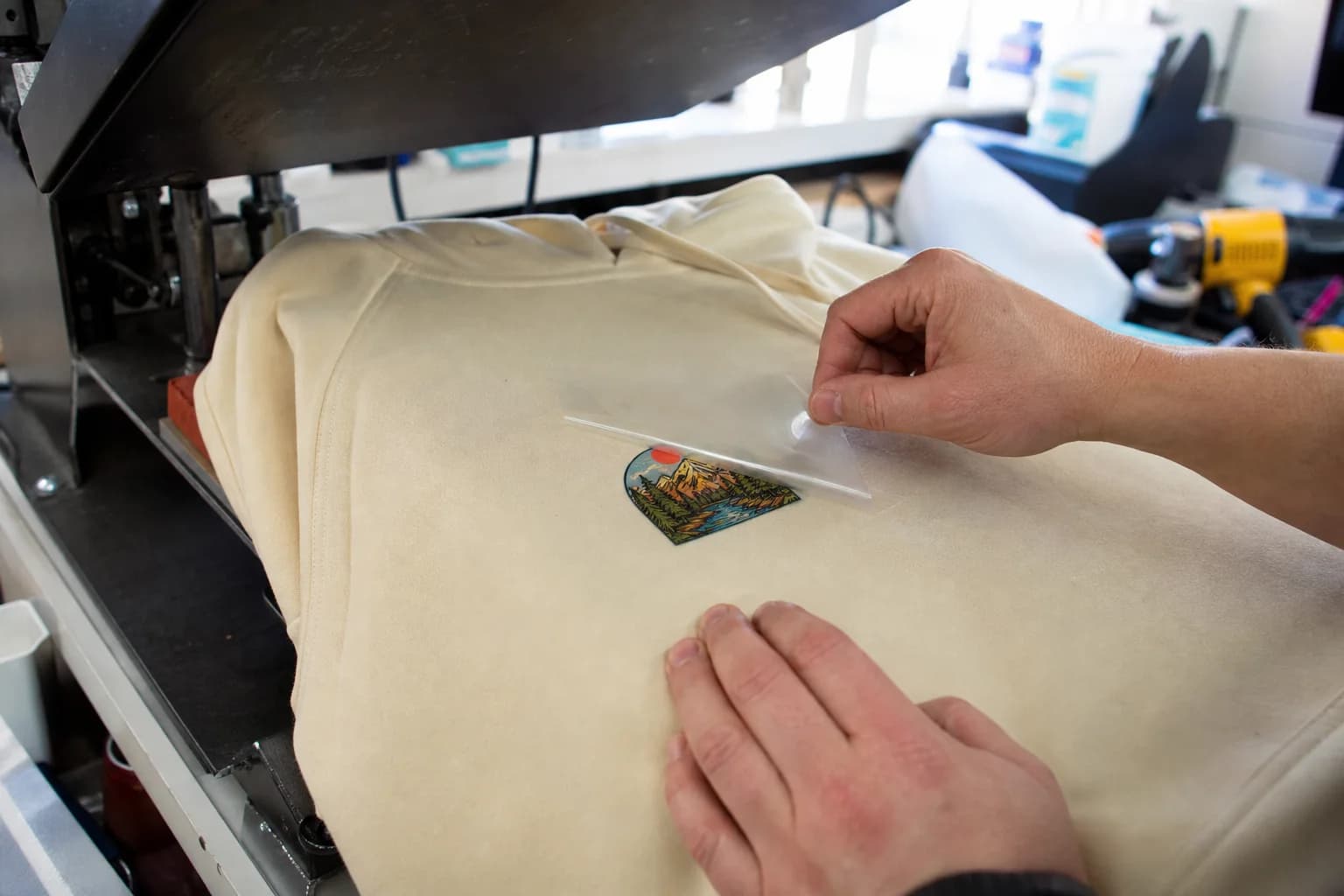 Print operator peeling a DTF carrier film from a printed black shirt