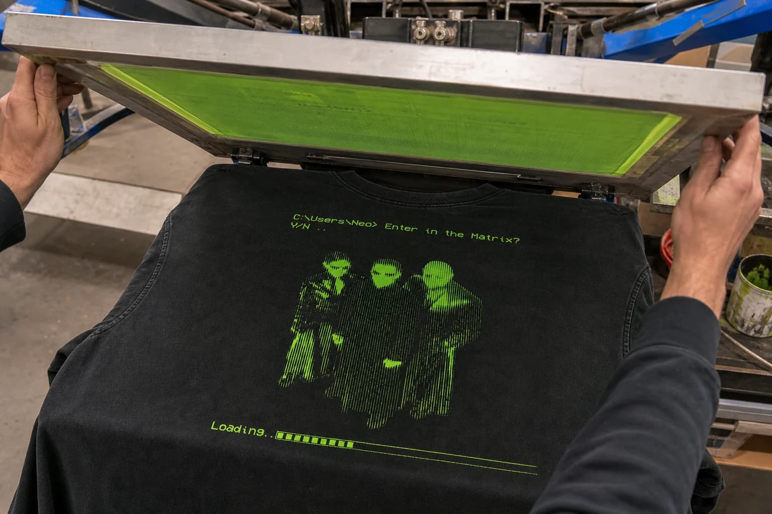 Screen-printing frame being lifted to reveal a detailed print on a black shirt