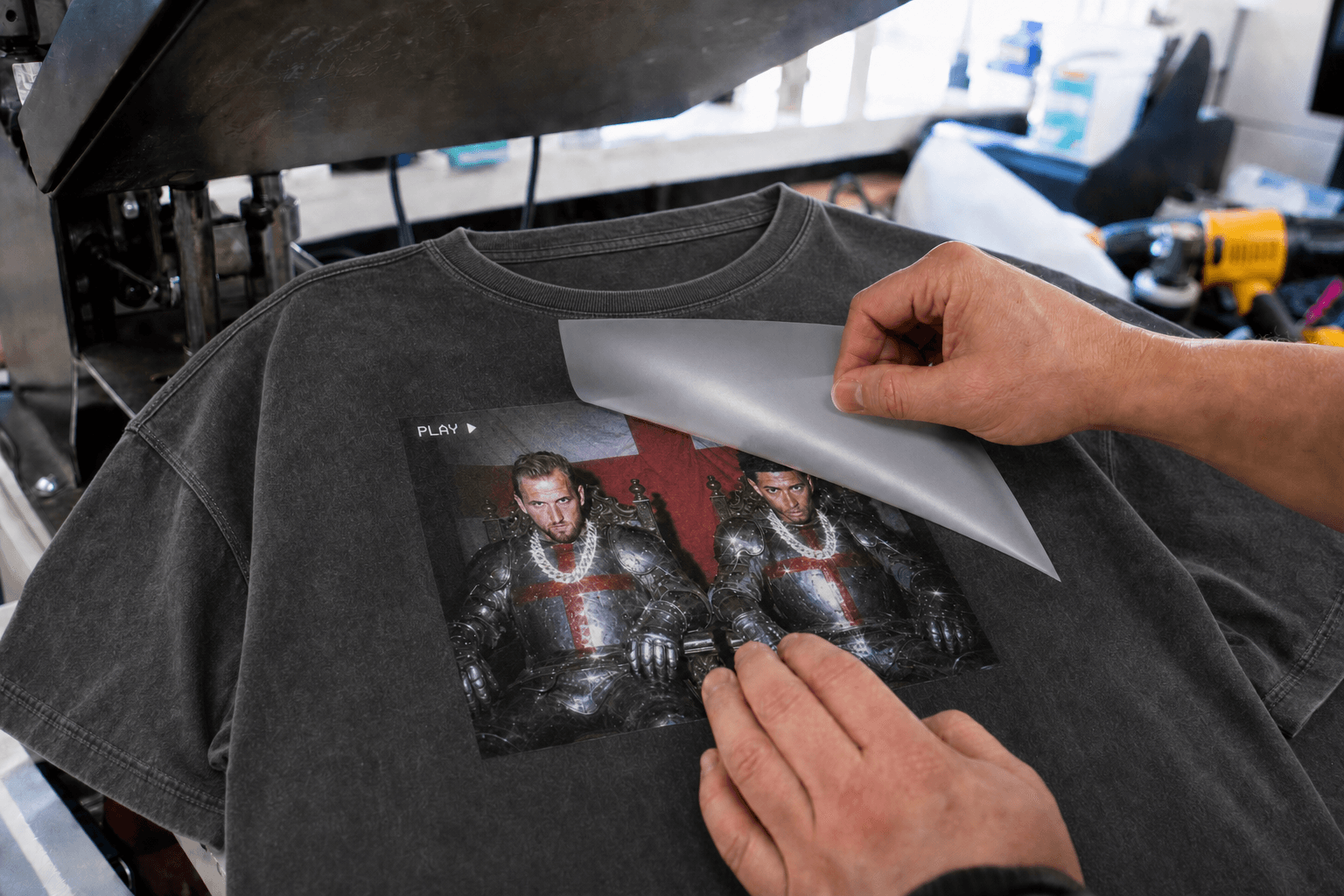 Operator peeling a DTF carrier from a washed black graphic T-shirt