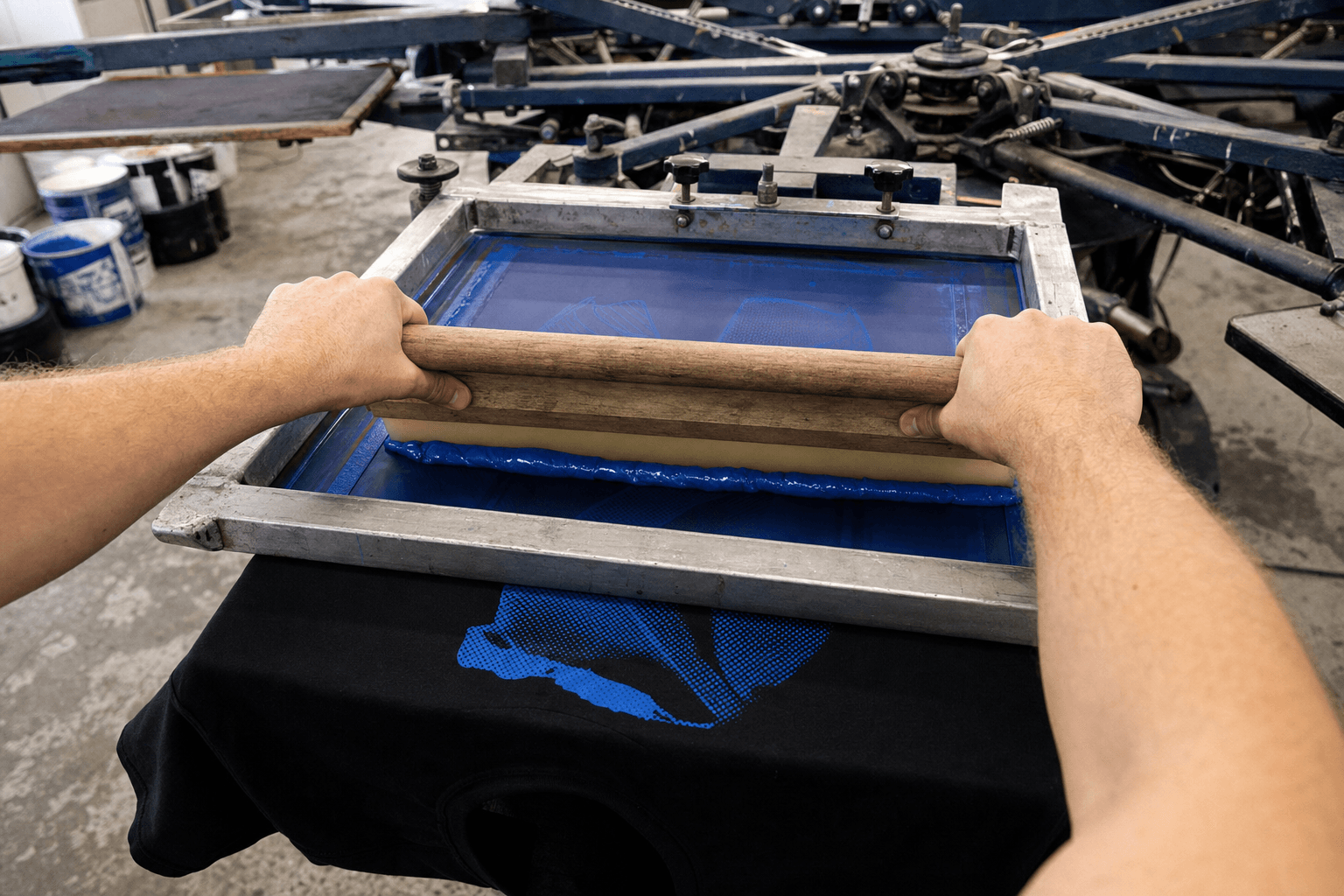 Printer pulling blue ink through a screen on a manual press
